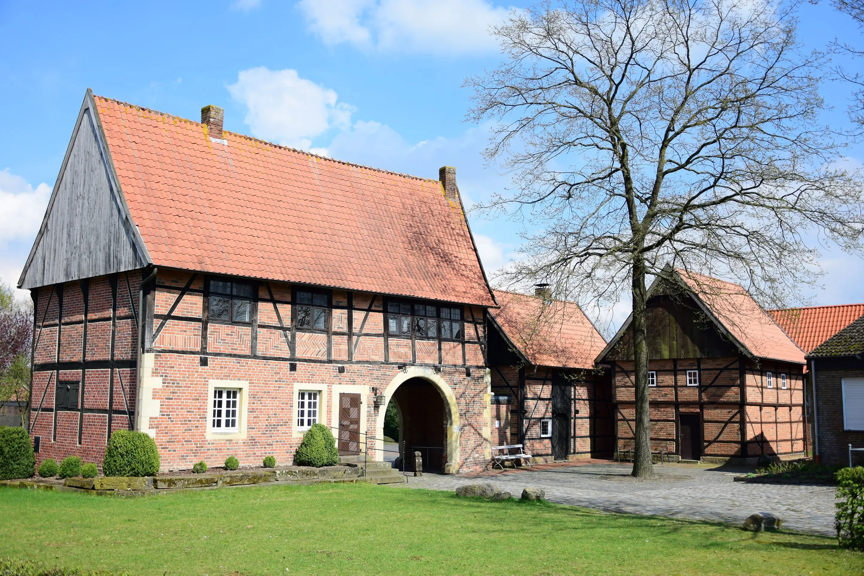 Torhaus mit Rundbogen am Stift Asbeck in Legden, daneben Fachwerkgebäude und ein kahler Baum