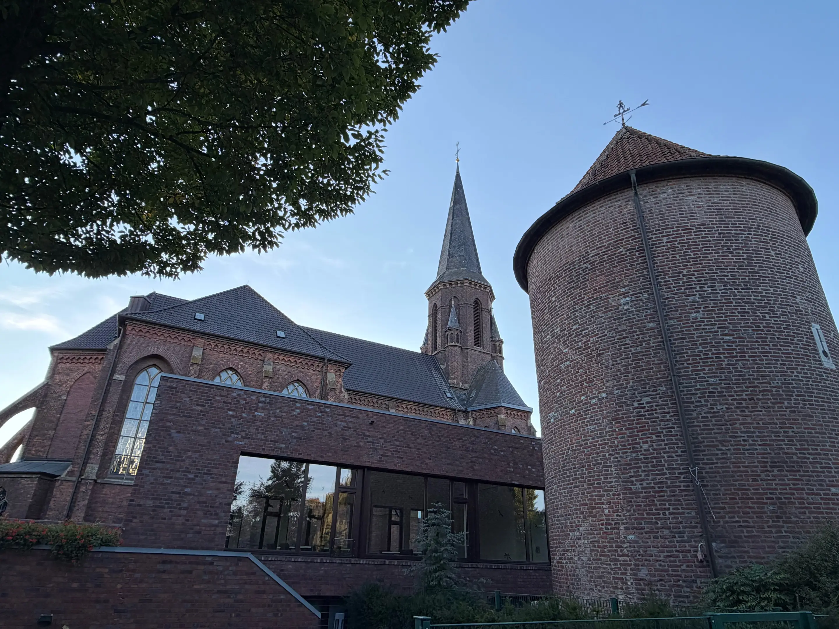 Runder Backstein-Stadtturm und Kirchturm in Isselburg vor blauem Himmel